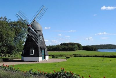 "Charmante Windmühle in Dänemark vor blauem Himmel, umgeben von grünen Wiesen." Titel-Attribut: