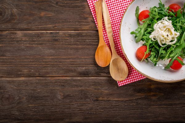 Ein gedeckter Holztisch mit Pasta, Tomaten und Basilikum – Italienisch lernen leicht gemacht mit Ich-Nix-Verstehen.de. Das Wort Tisch heißt auf Italienisch Tavolo.